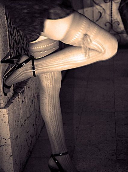 A leg in patterned tights and heels raised against a wall.