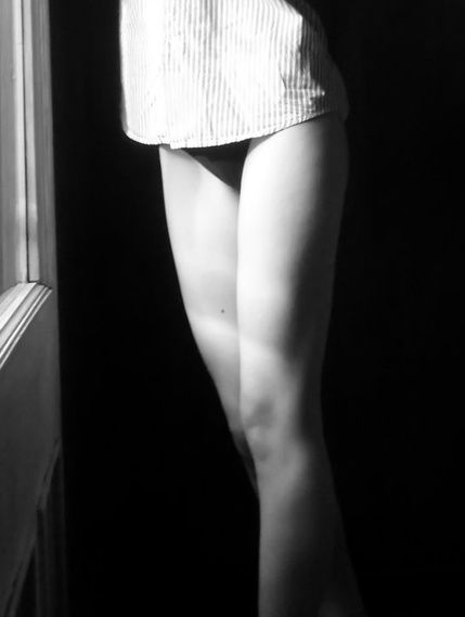 Legs under a light dress beside a dark doorway, in black and white.