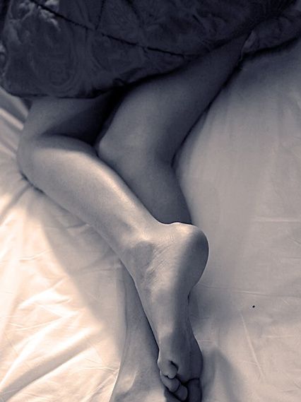 A bare leg and foot resting on a white sheet.
