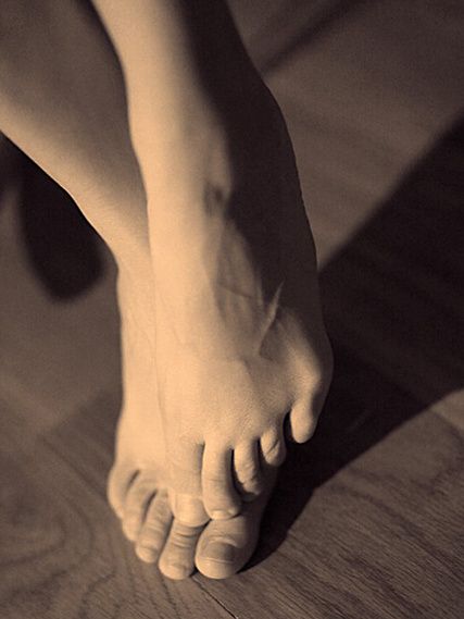 A bare foot on tiptoe on a wooden floor, in warm sepia.