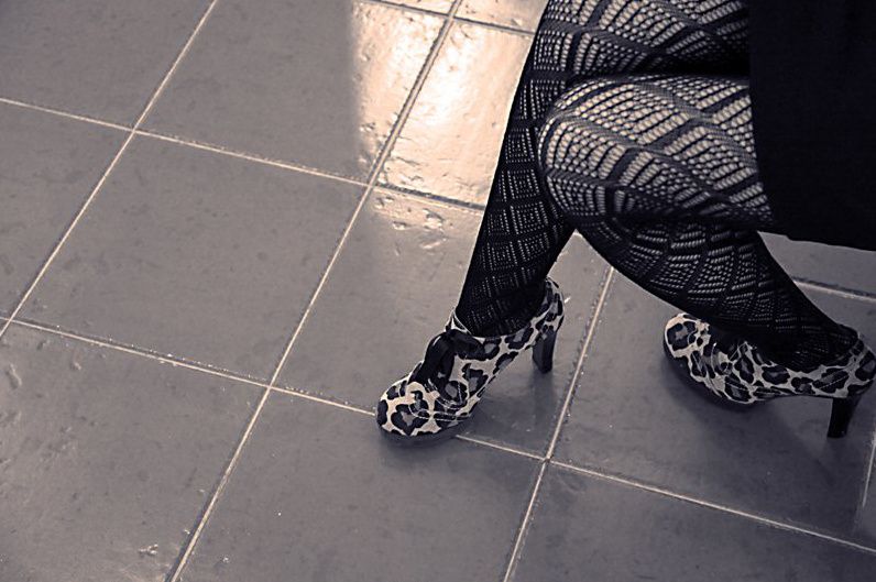 Crossed legs in black lace tights and leopard-print heels on a tiled floor.