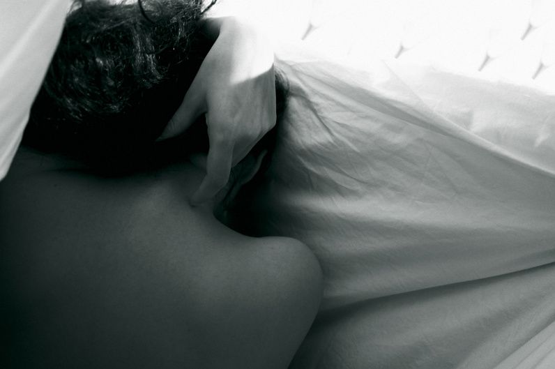 A bare back and dark hair half hidden under a white sheet.