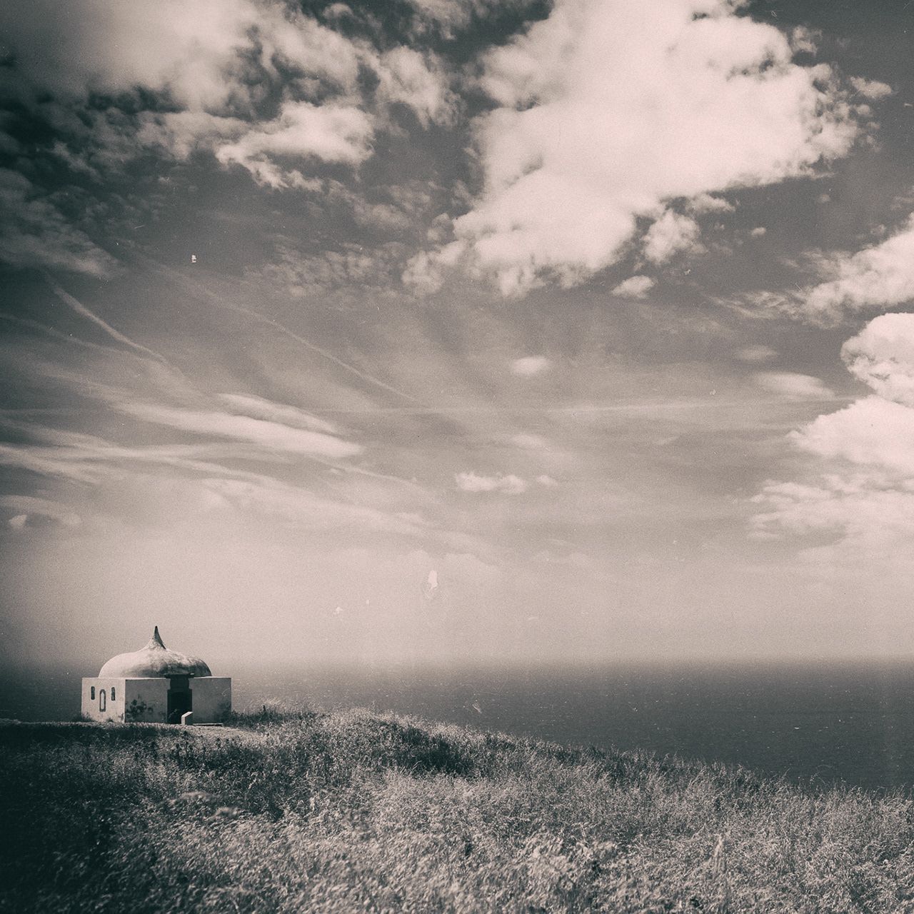 Small white chapel on a grassy cliff above the Atlantic, under a wide sky of clouds.