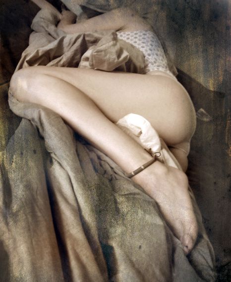 A nude curled up on folds of brown fabric, an anklet at her foot.