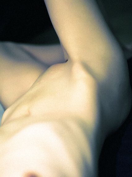 A nude lying back with one arm raised, lit from above against black.