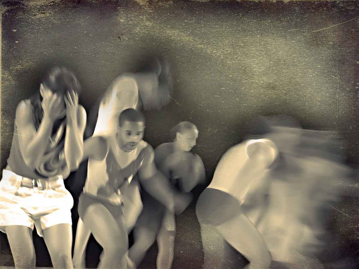 Four dancers in a row, blurred in motion, one with hands over his face, in faded black and white.