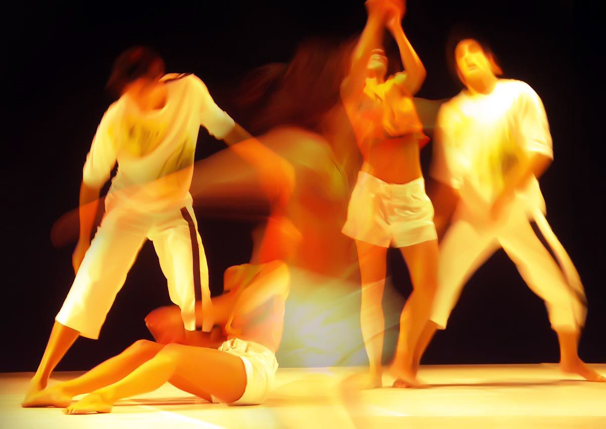 Dancers in white lit in hot orange, one lying on the floor, the others leaping above.