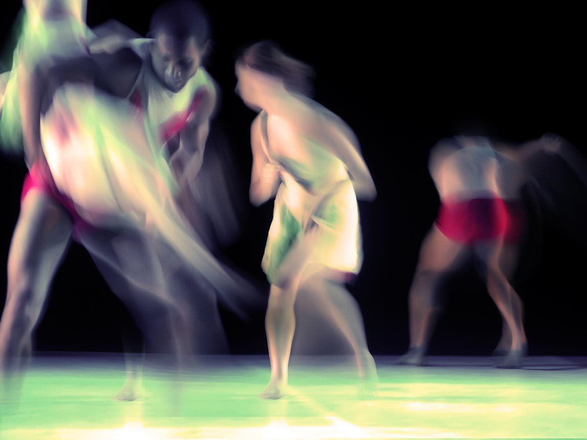 Dancers blurred across a green-lit stage, trails of pink and violet.