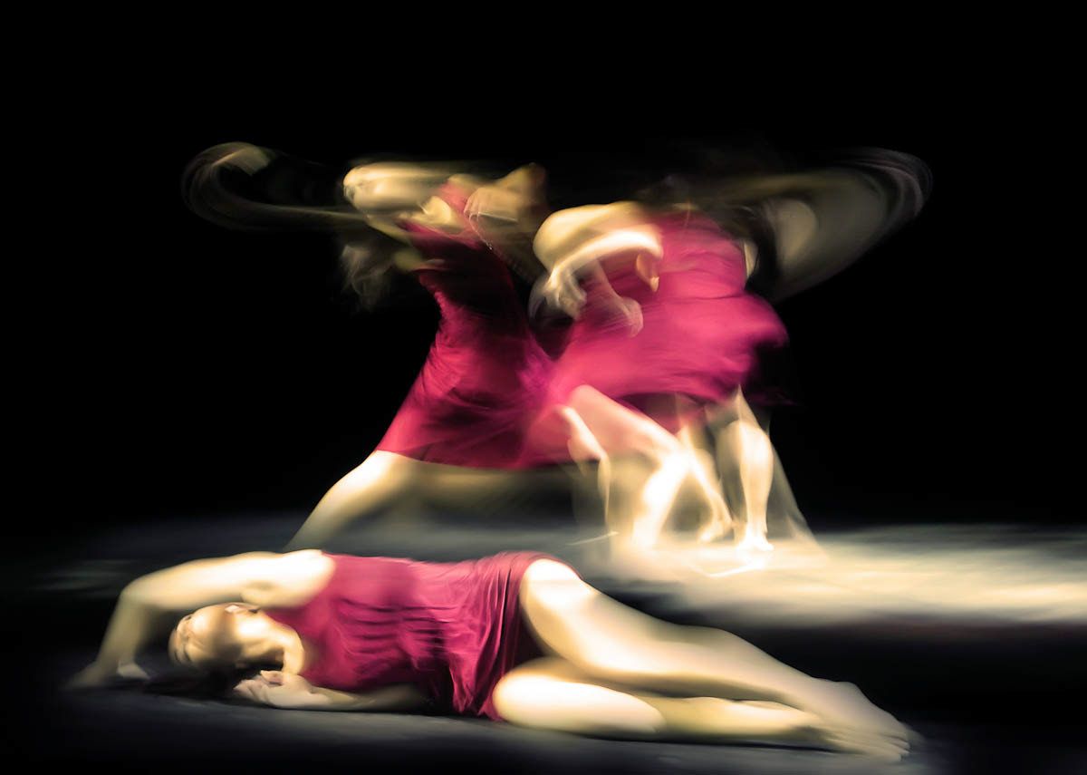 Two dancers in magenta, one lying on the floor, the other twisting above in motion blur.