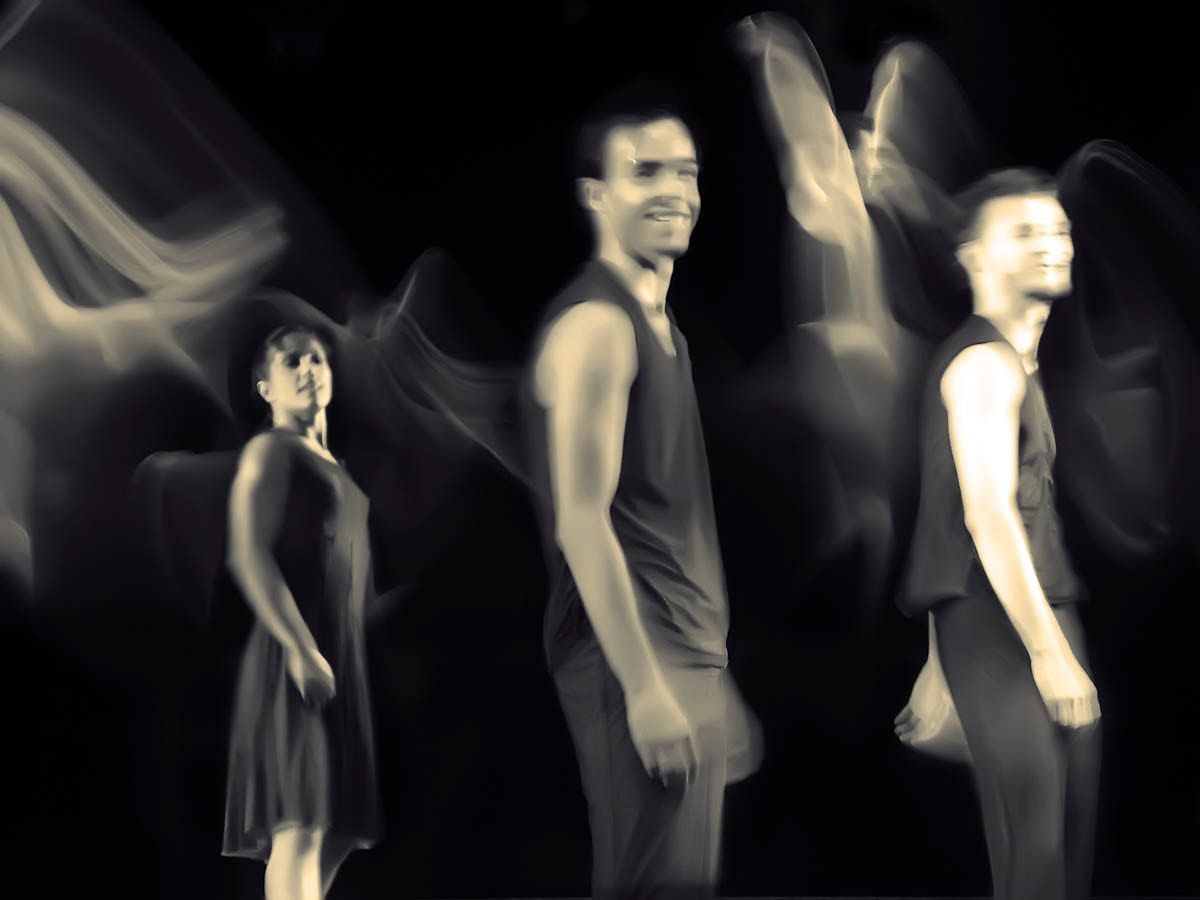 Three dancers in black and white, faces sharp, arms dissolving into motion.