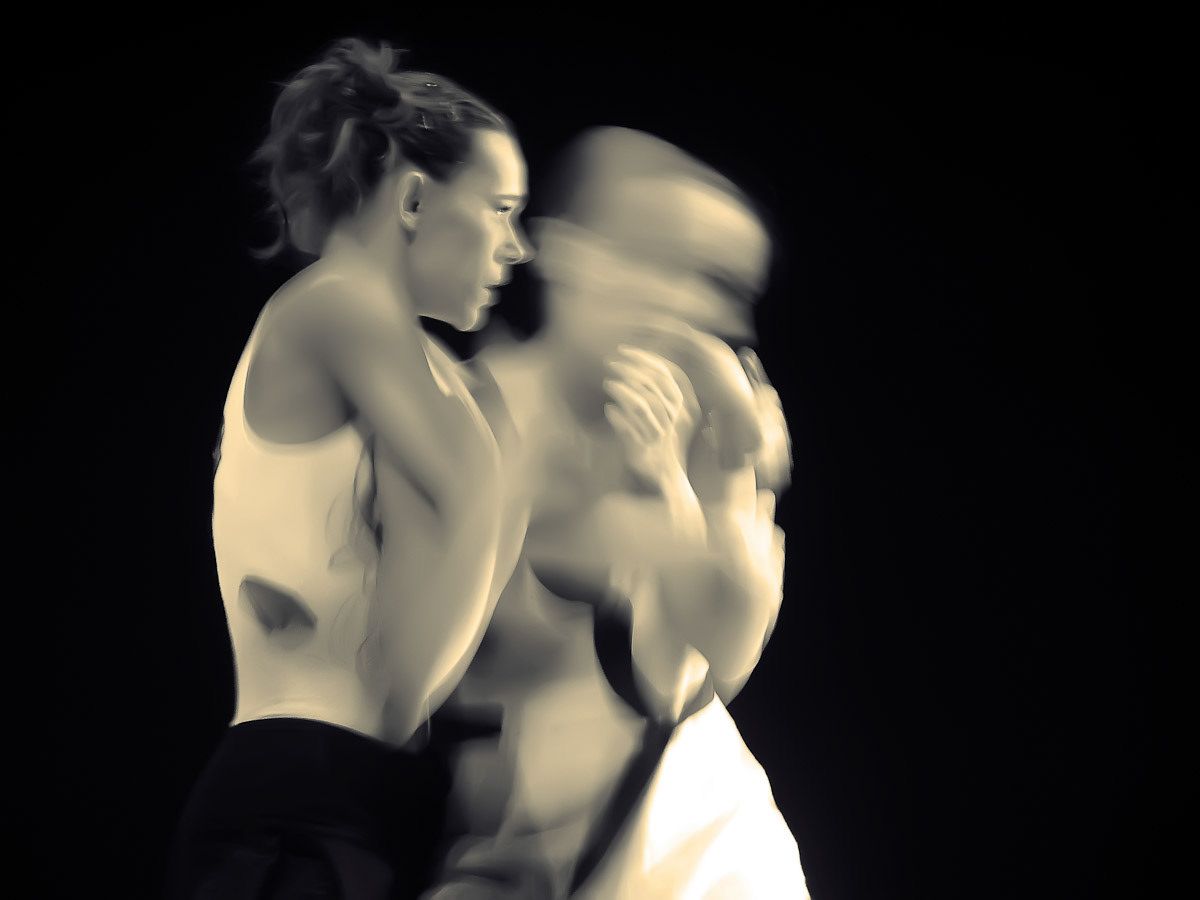 Two dancers in black and white, one sharp, one blurred, close together.