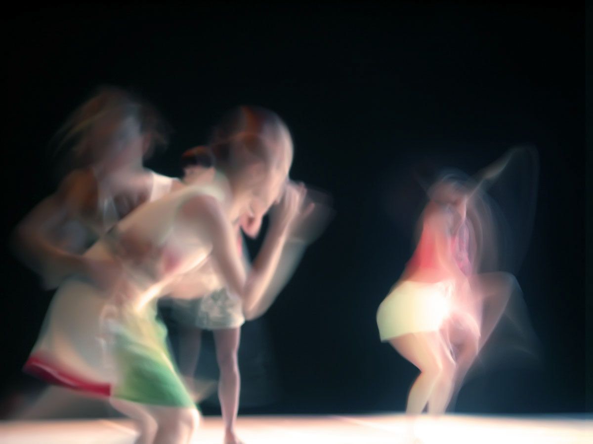 Dancers bending and spinning in soft blurred pastels against black.