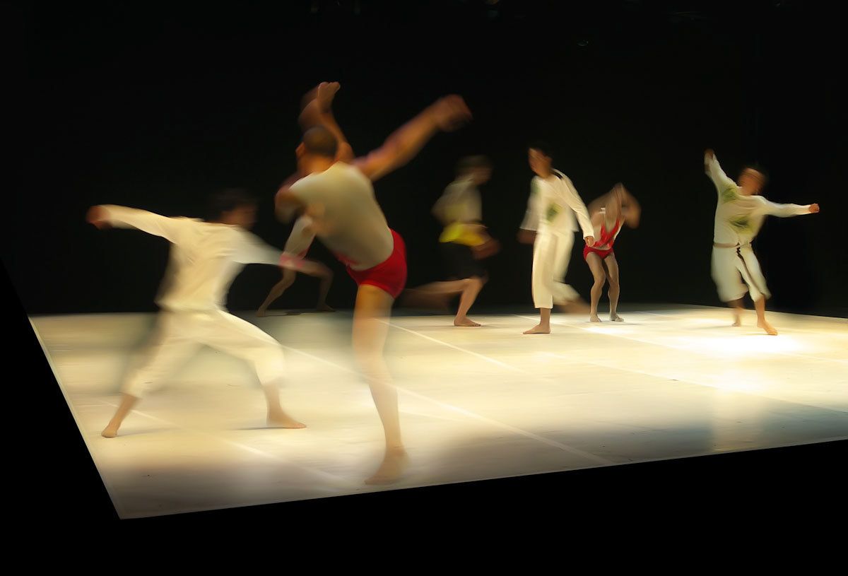 A wide stage with dancers in white leaping and stretching in a line.