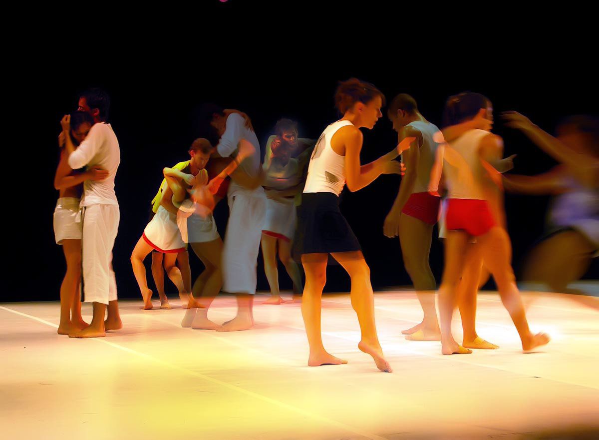 A crowd of dancers in casual clothes walking and embracing on a bright stage.
