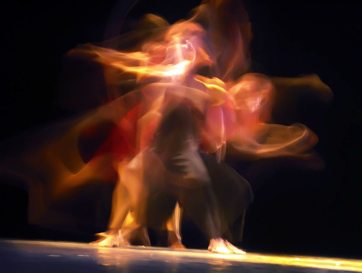 Dancers in long exposure, bodies turned to flame-like trails of orange and red.