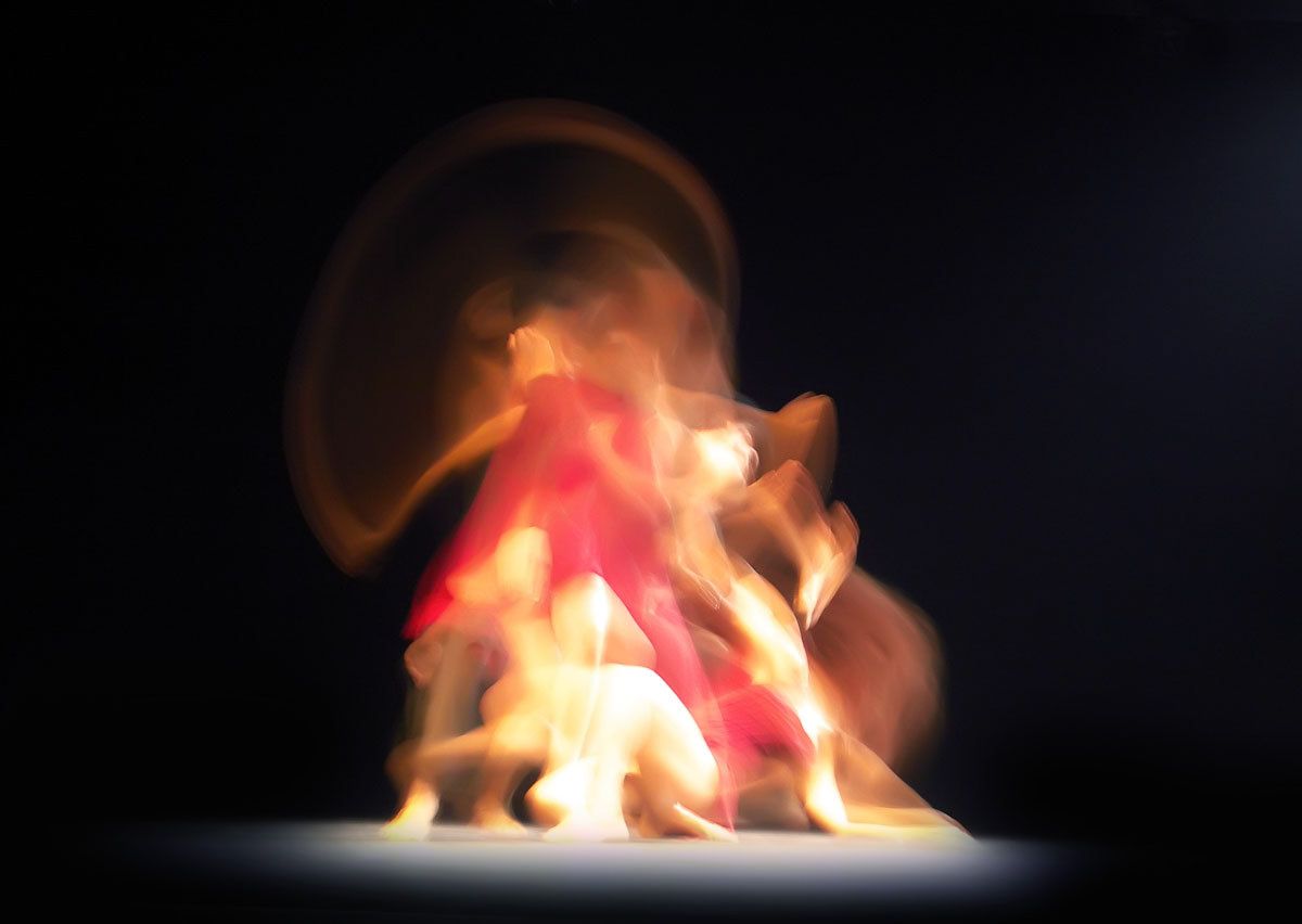 A cluster of dancers spinning into a halo of red and orange light.