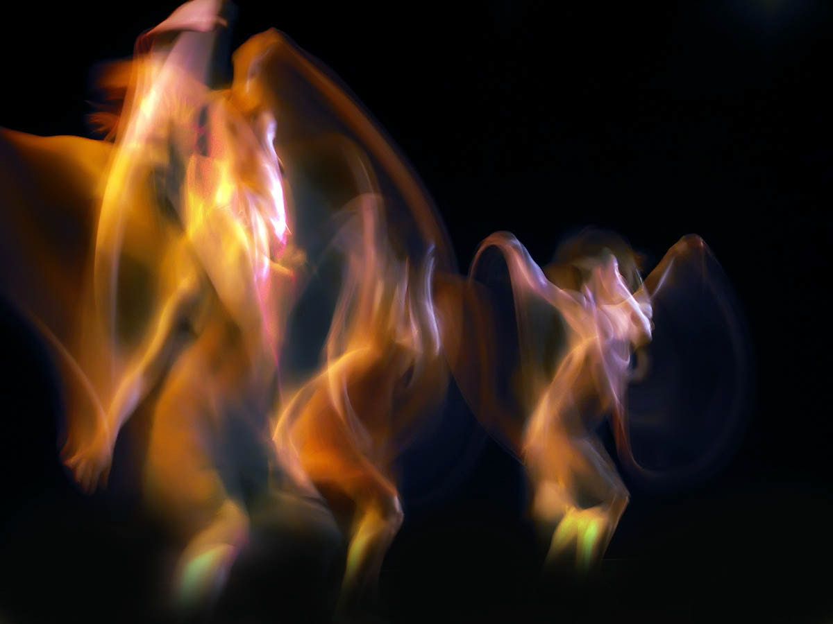 Flame-like trails of orange and violet left by leaping dancers against black.