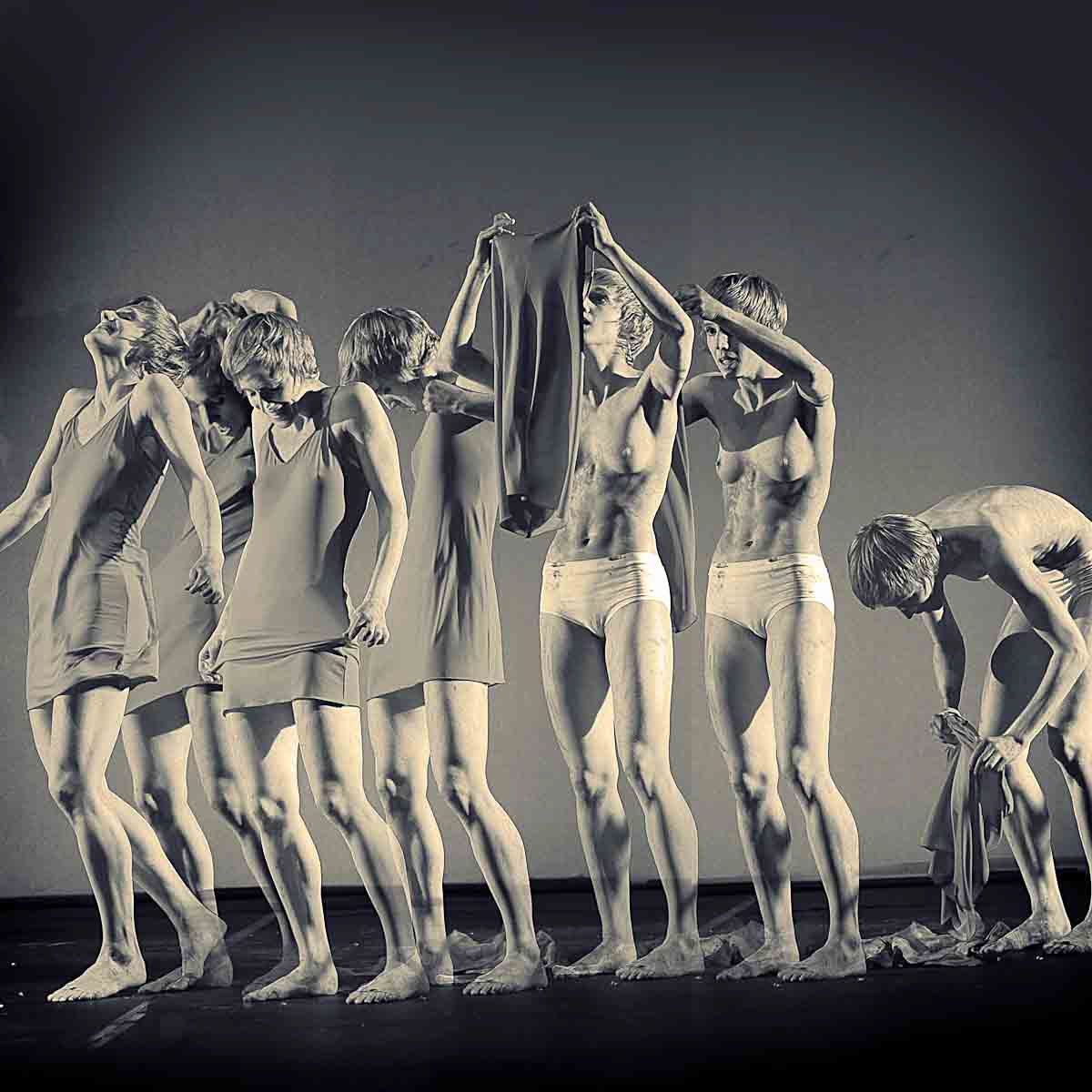A row of dancers in sepia, arms raised, one bending forward at the edge of the frame.