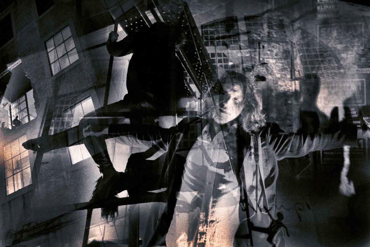 A woman with outstretched arms among climbing figures, windows and ladders, in black and white.