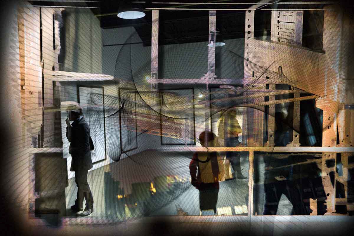 People walking through a layered space of scaffolding, mesh and coloured light.