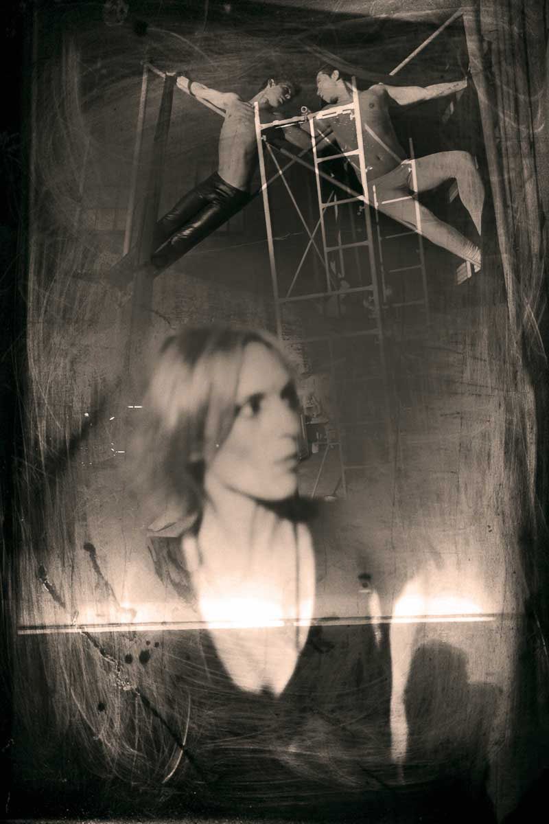 A woman's face below two acrobats on a ladder, in a scratched, glowing print.