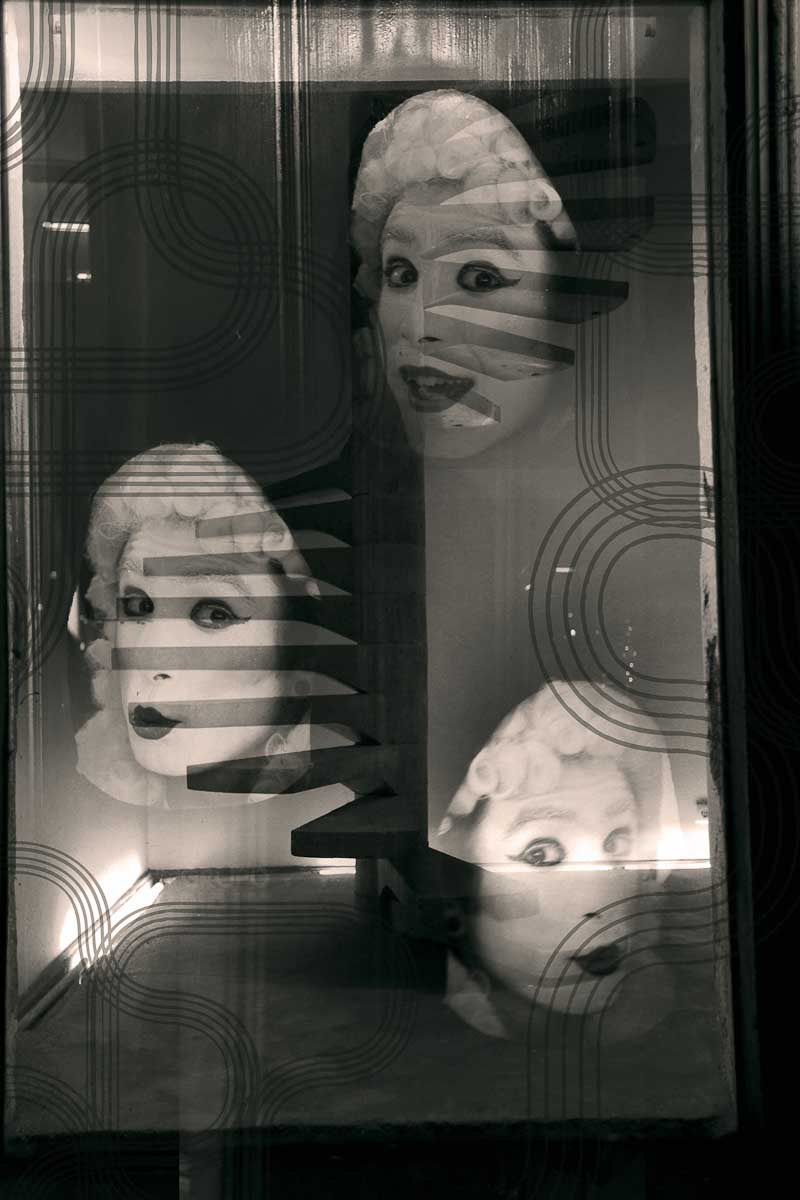 Three mannequin heads with startled faces behind striped glass.