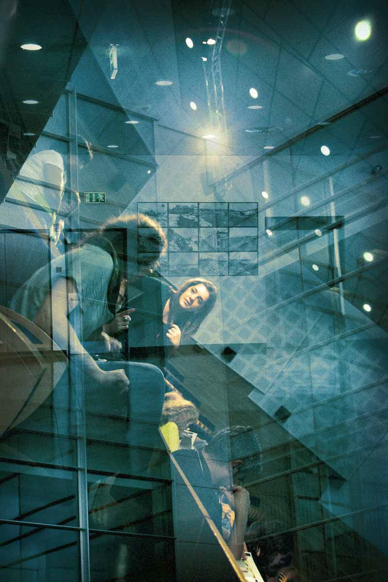 People on a staircase seen through layers of blue-green glass and light.