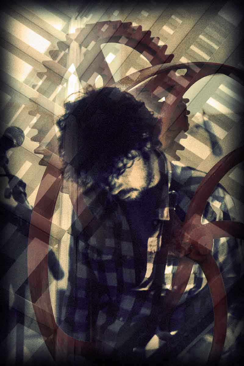 A young man with curly hair bowed among large red gears.