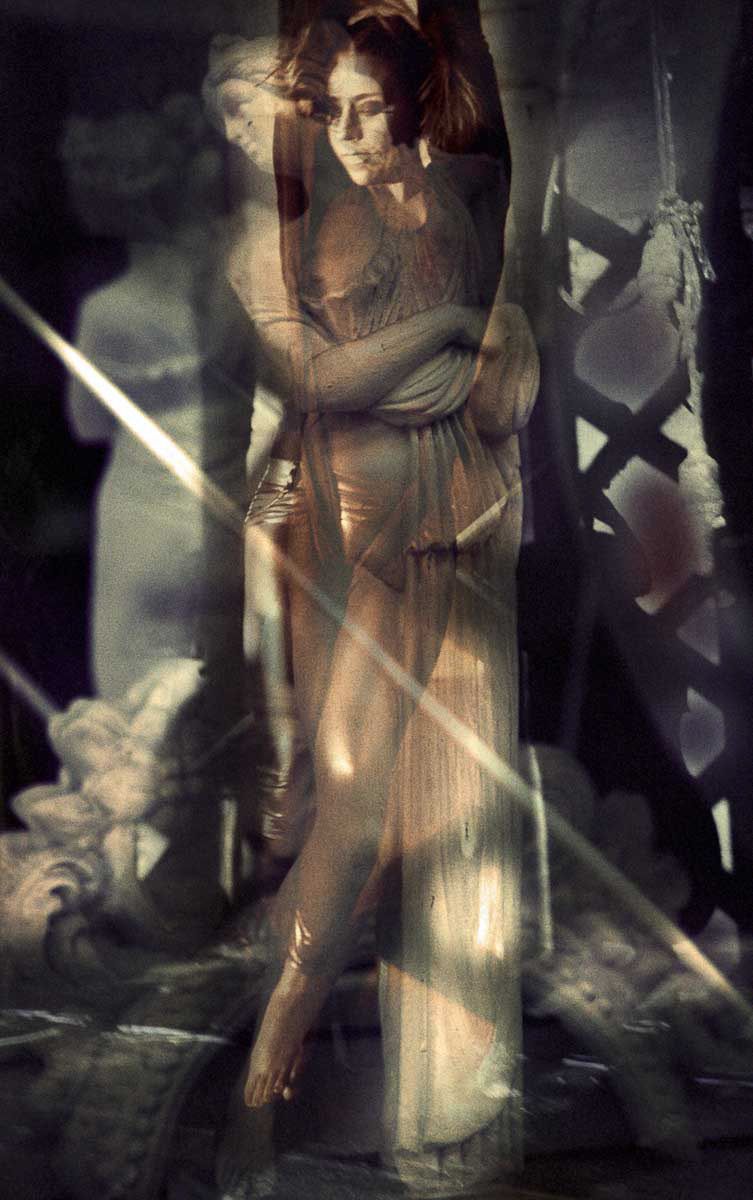 A woman in a sheer dress among statues and rays of light.
