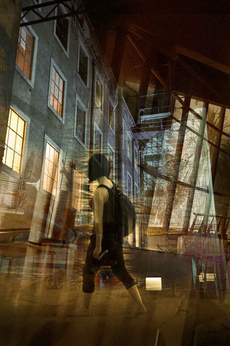 A woman walking past a lit building, overlaid with steel beams, in amber.