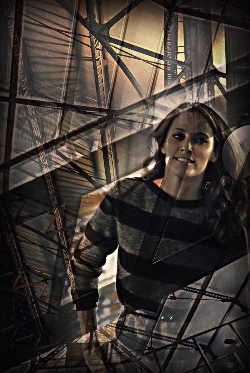 A smiling woman in a striped sweater framed by steel girders.