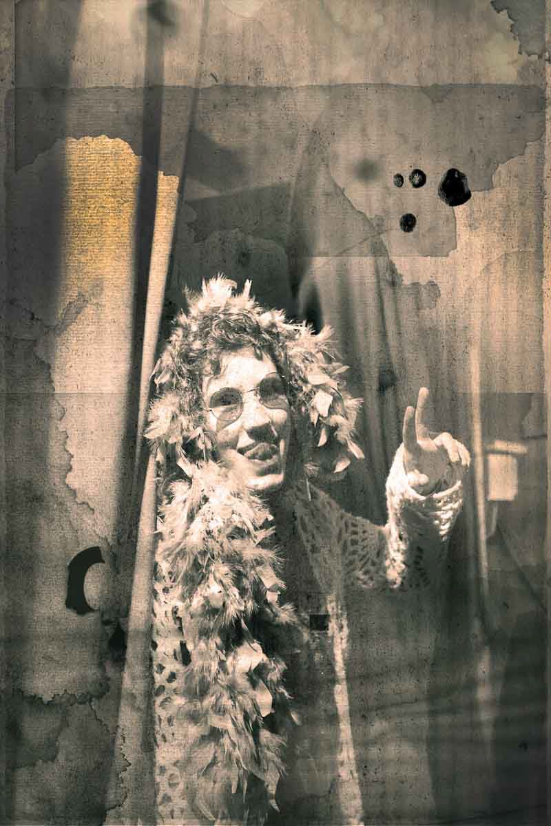 A smiling performer in a feather boa against a stained, faded wall.