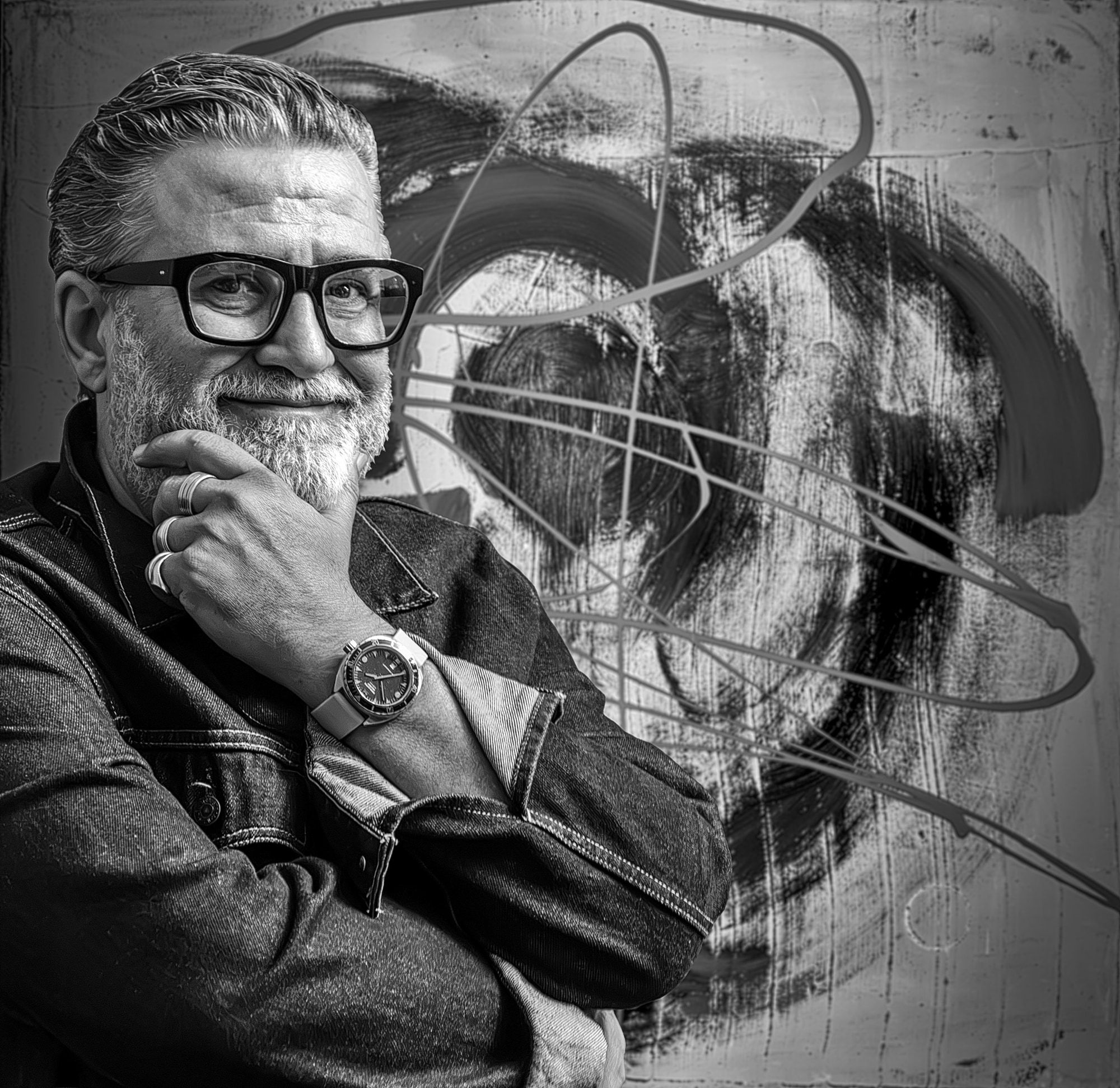 Portret alb-negru al lui Dan St. Andrei, cu ochelari și geacă de denim, cu mâna la bărbie, în fața unei picturi gestuale mari care înfățișează un chip.