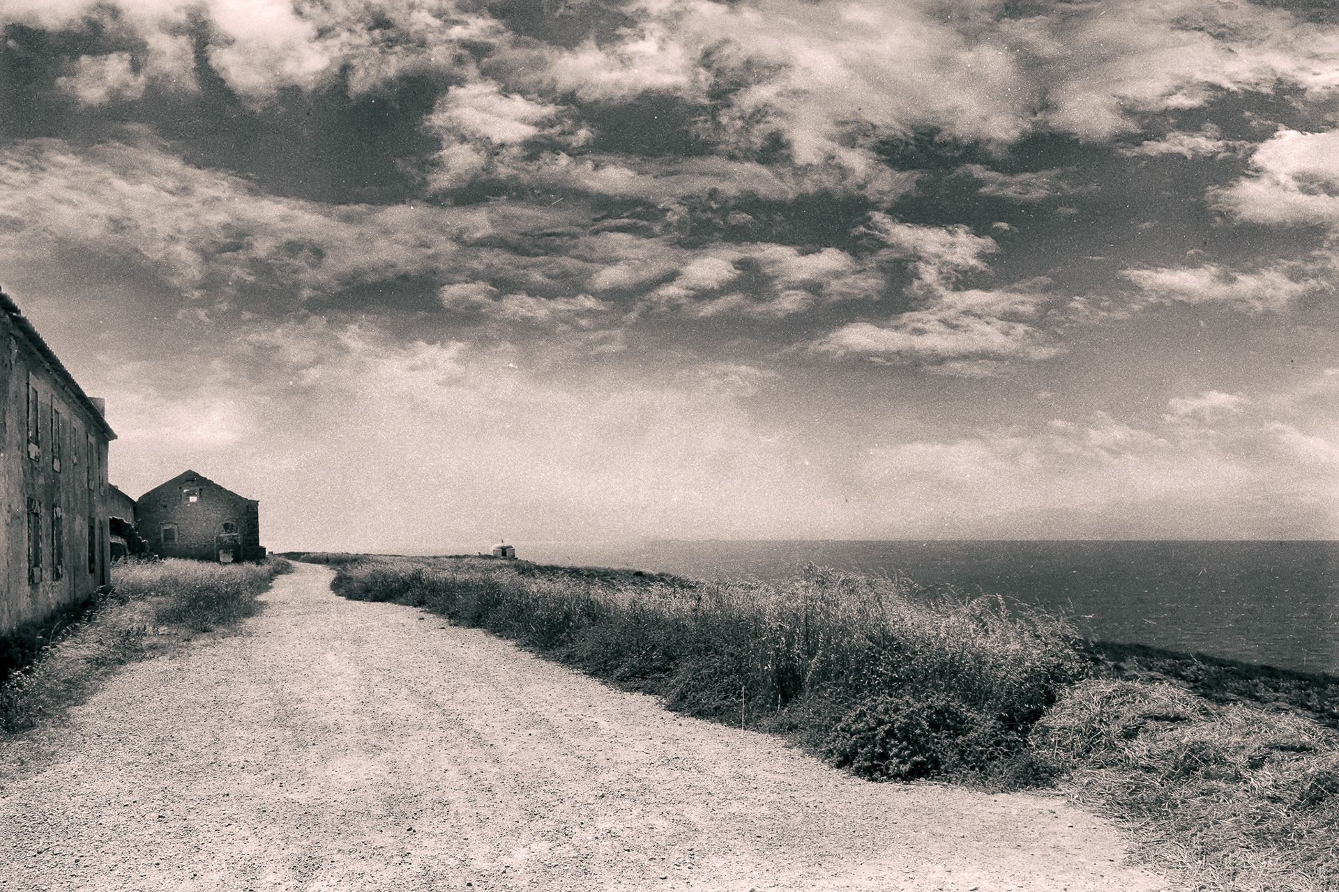 A gravel path along a grassy cliff top beside low stone buildings, the sea on the right.