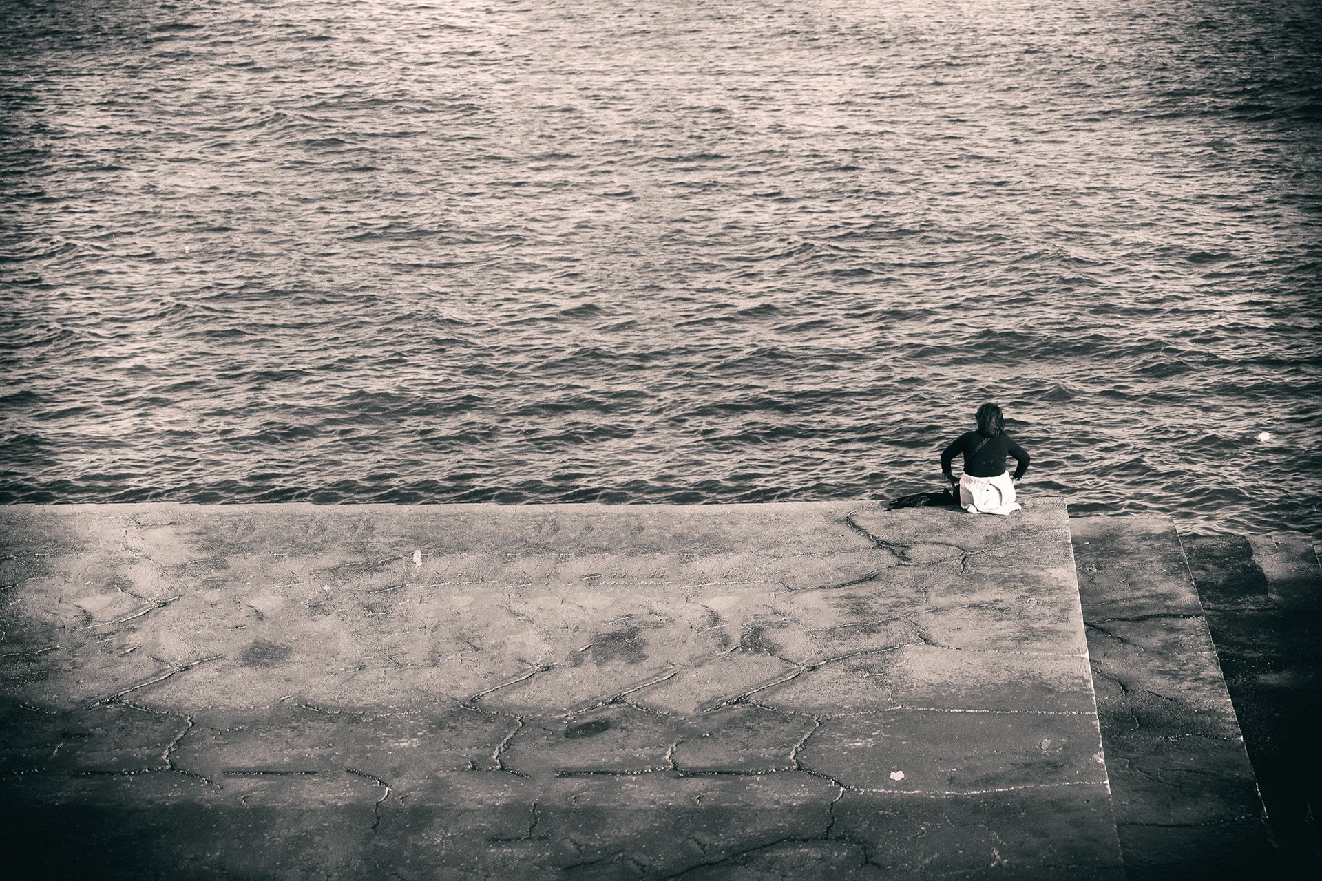 A person sitting at the edge of a concrete platform above a rippled sea.
