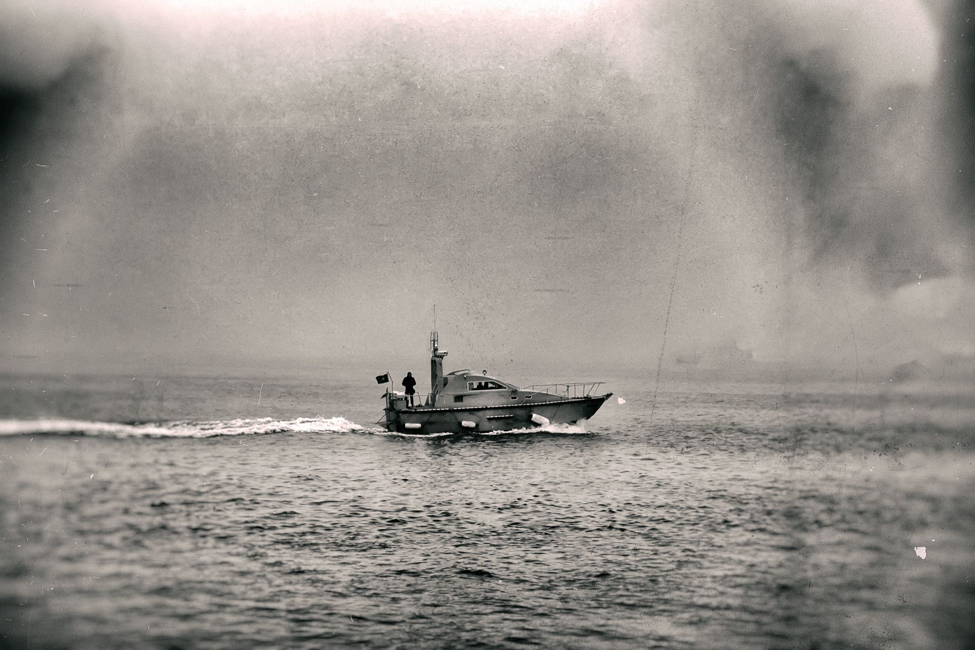 A motorboat crossing a misty sea, leaving a trail of white wake.
