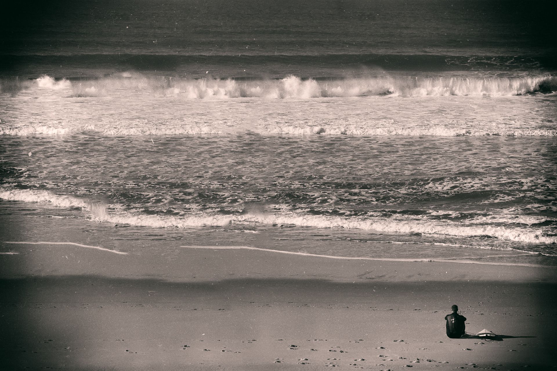 A person sitting alone on the sand facing rolling waves.