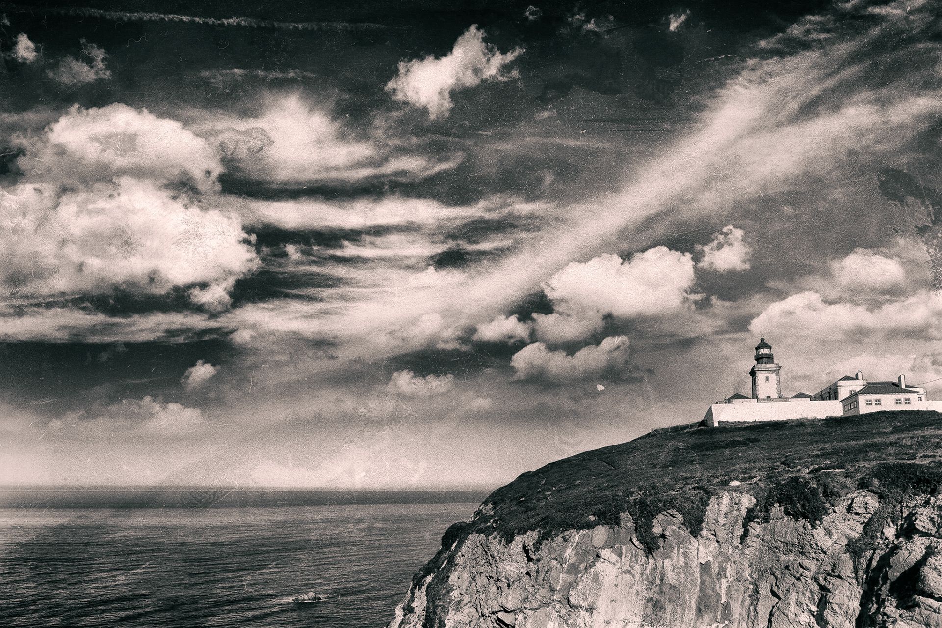 A lighthouse on a white cliff edge above the sea, under streaks of cloud.