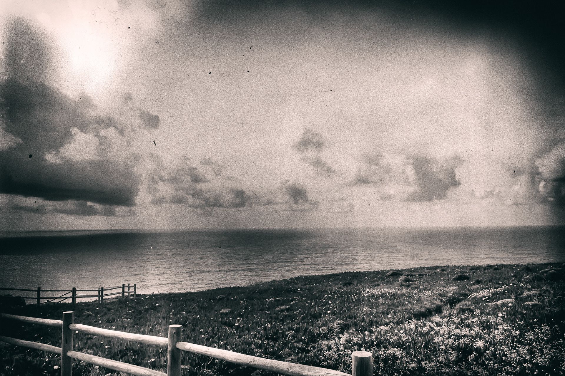 A wooden fence along a grassy clifftop overlooking a hazy sea.