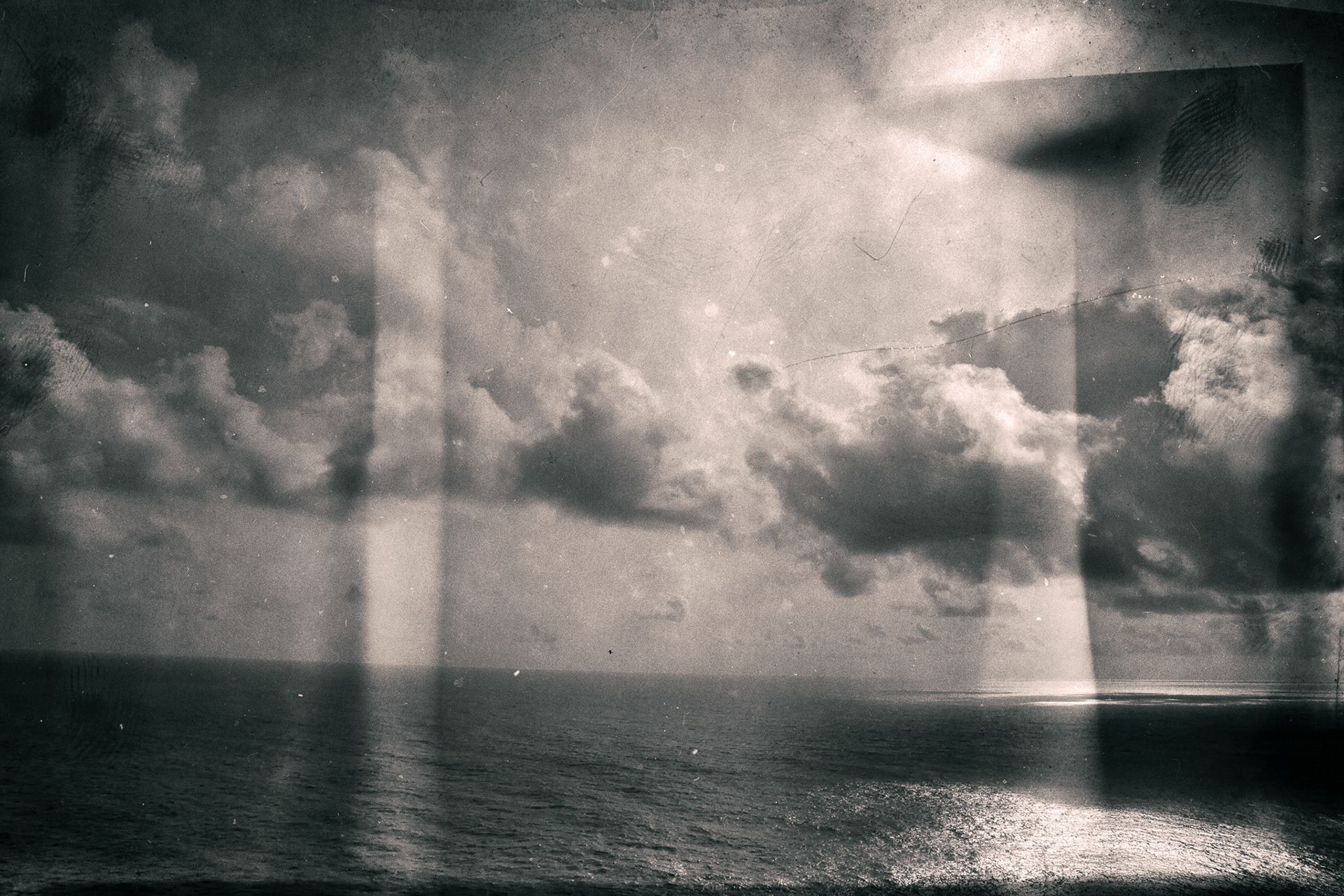 Shafts of light falling through clouds onto a calm sea, with faded film marks.