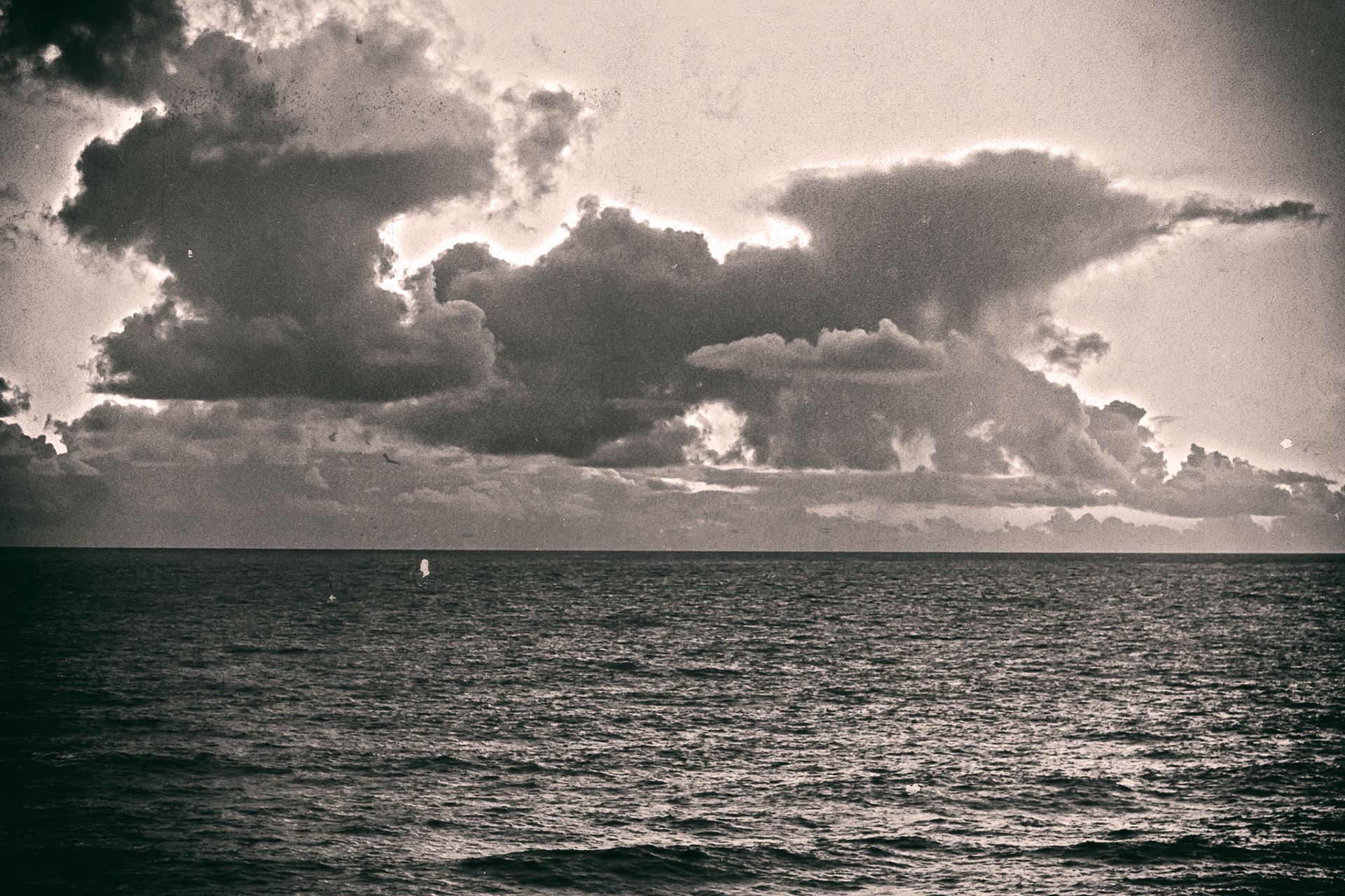 Towering clouds lit from behind above a dark, rippled sea.