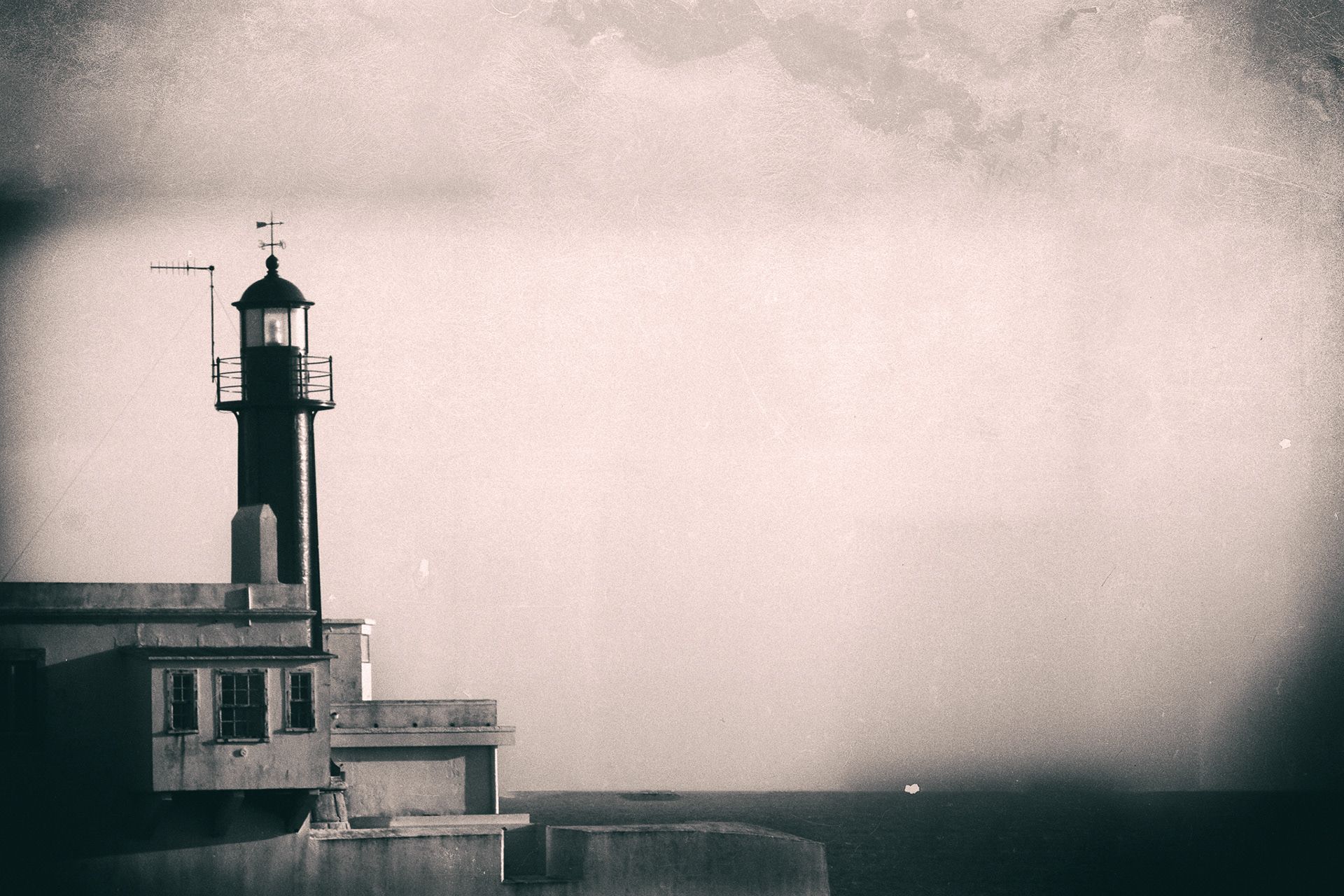 A lighthouse tower rising from a harbour building against a pale sky.