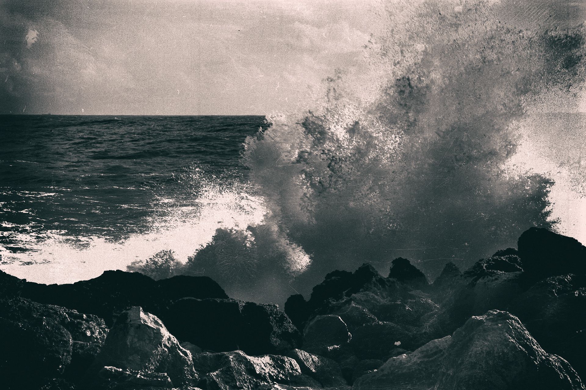 A huge wave exploding in spray against dark rocks.