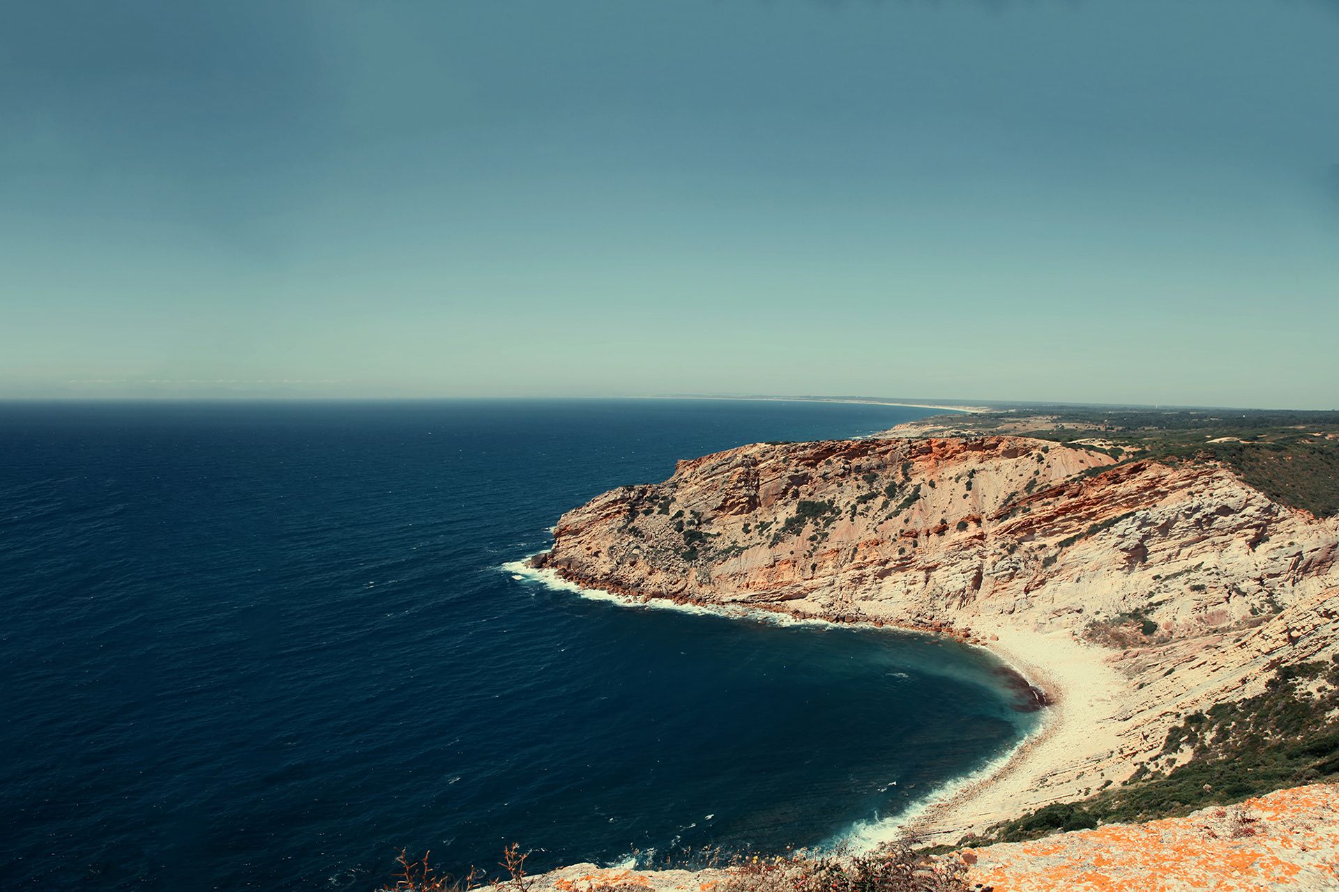 A curved cove of pale cliffs closing around a deep blue bay, in colour.